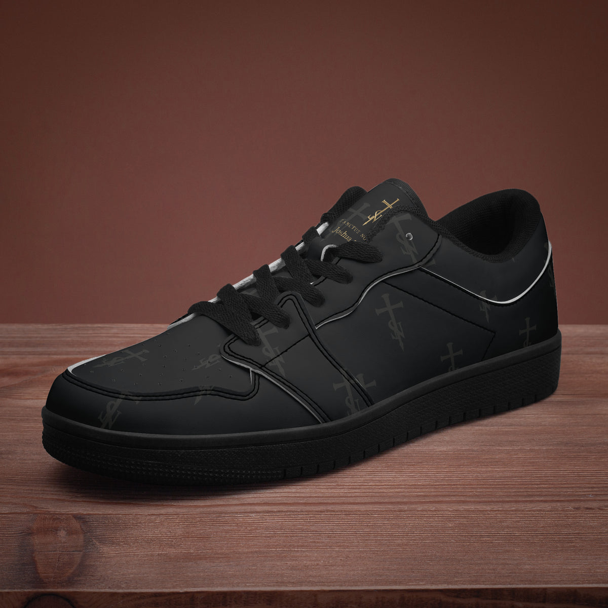 SANCTUS NOVA Deep Black low-top sneaker with tonal cross-and-SN print, shown at an angle on a wooden surface.